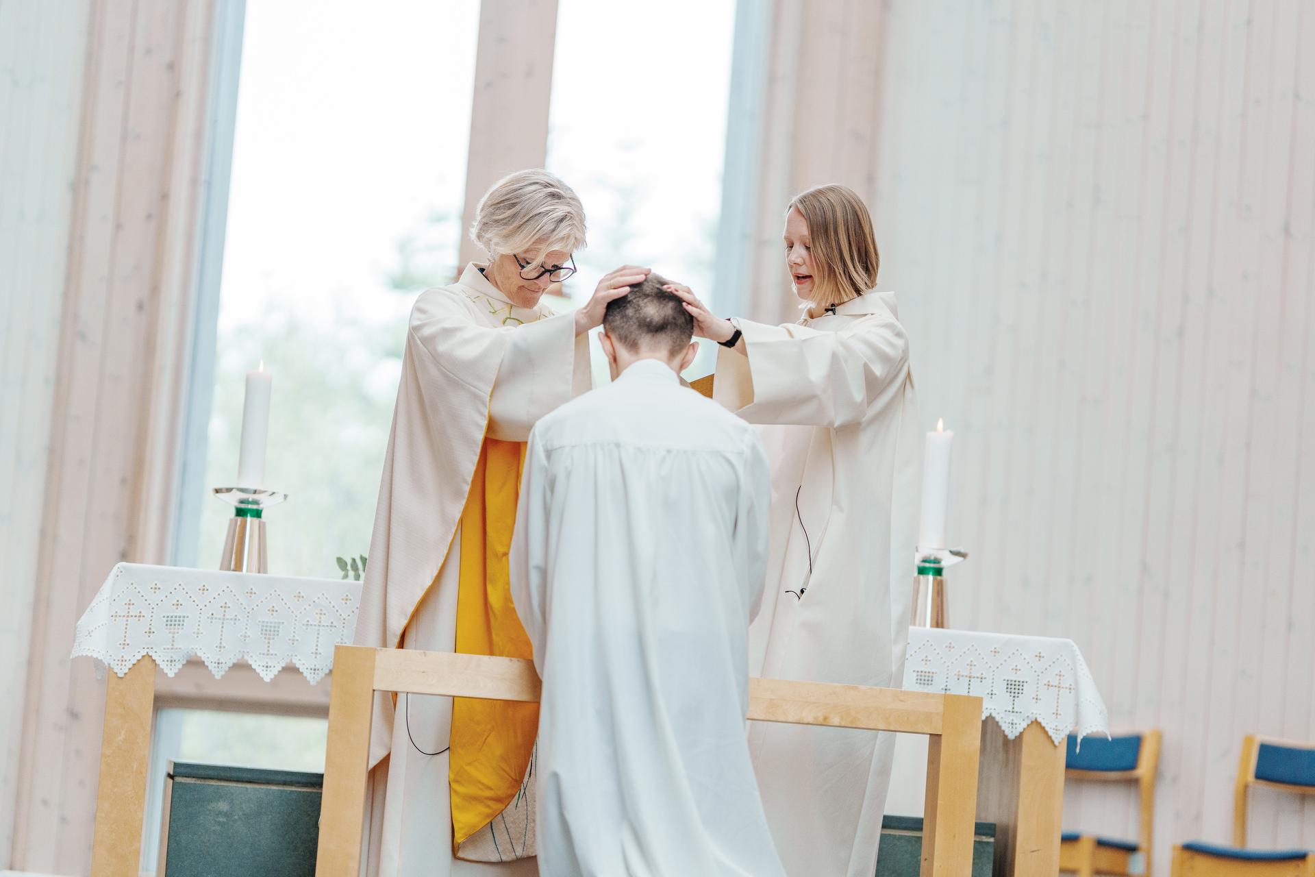 Konfirmant kneler på alterringen, blir bedt for at to i kyrkjestab
